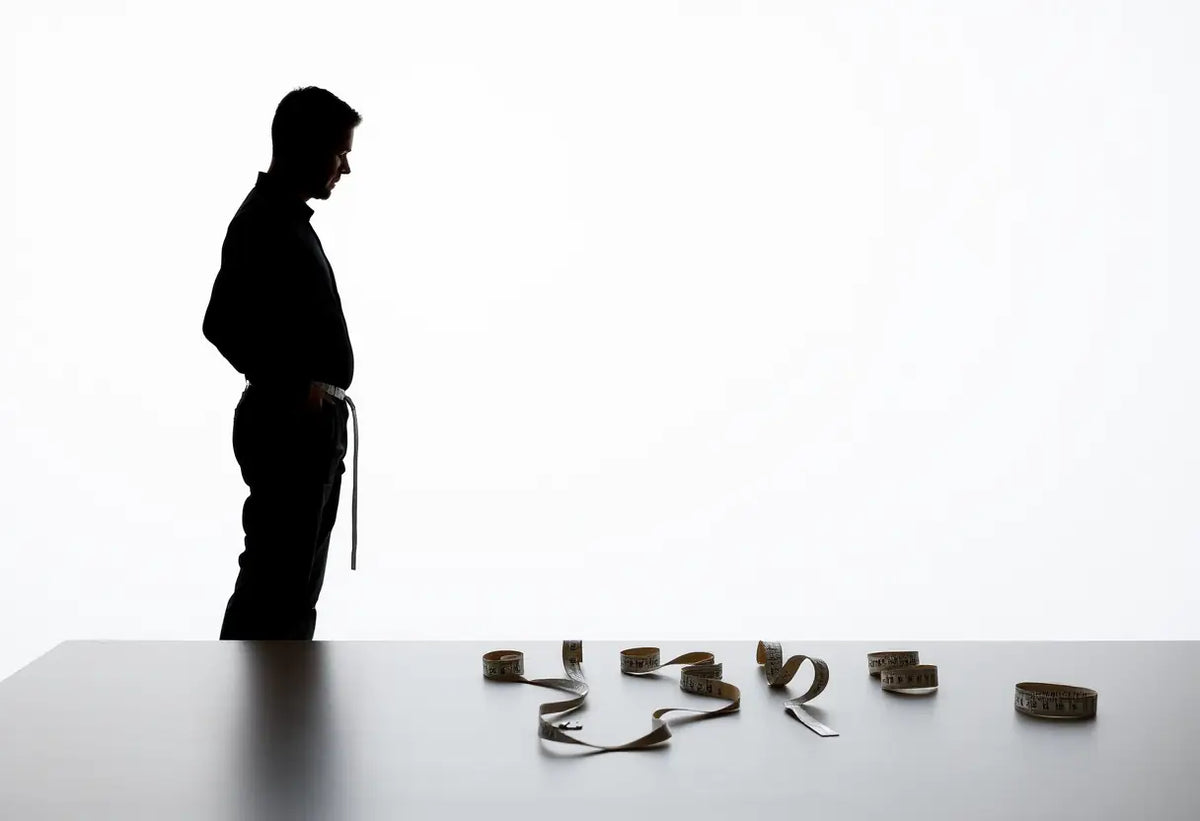 Un silhouetté d'homme se tient près d'une table où plusieurs rubans à mesurer la taille sont disposés.