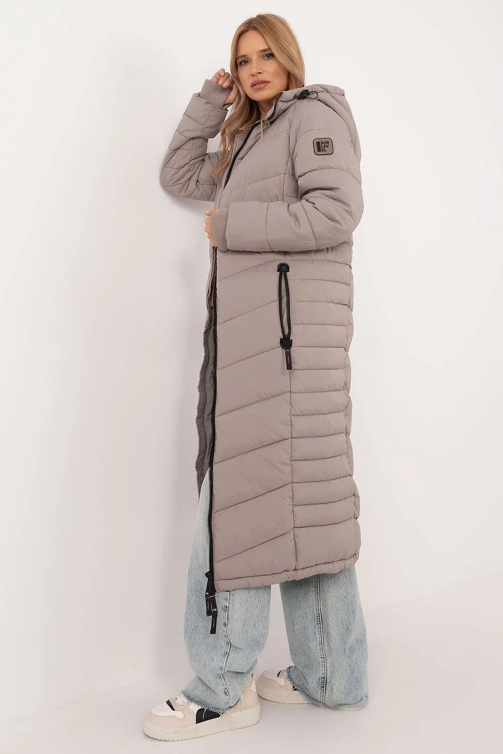 Veste matelassée longue pour femme en polyester, gris taupe, coupe ajustée, capuche, fermeture éclair, poches zippées, style moderne, hiver 2023