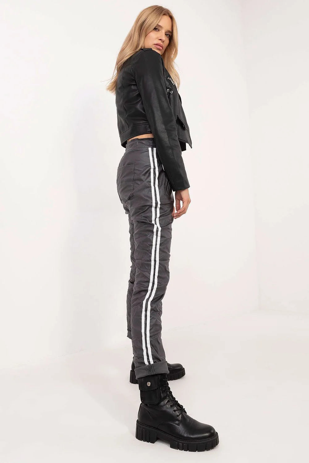 Veste cuir noir motard, top blanc court, pantalon gris ample, bottes noires robustes, ensemble moderne audacieux femme