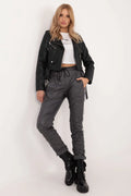 Veste cuir noir motard, top blanc court, pantalon gris ample, bottes noires robustes, ensemble moderne audacieux femme