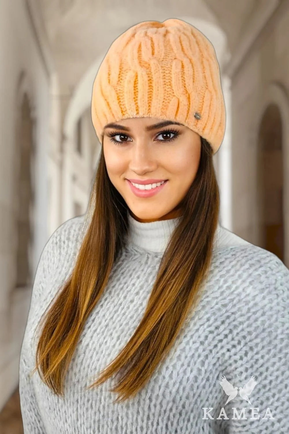 Bonnet féminin tricoté en torsades pêche douce, style classique, coupe ajustée, matériau doux, finitions soignées, logo métallique discret, vêtement hiver, mode intemporelle