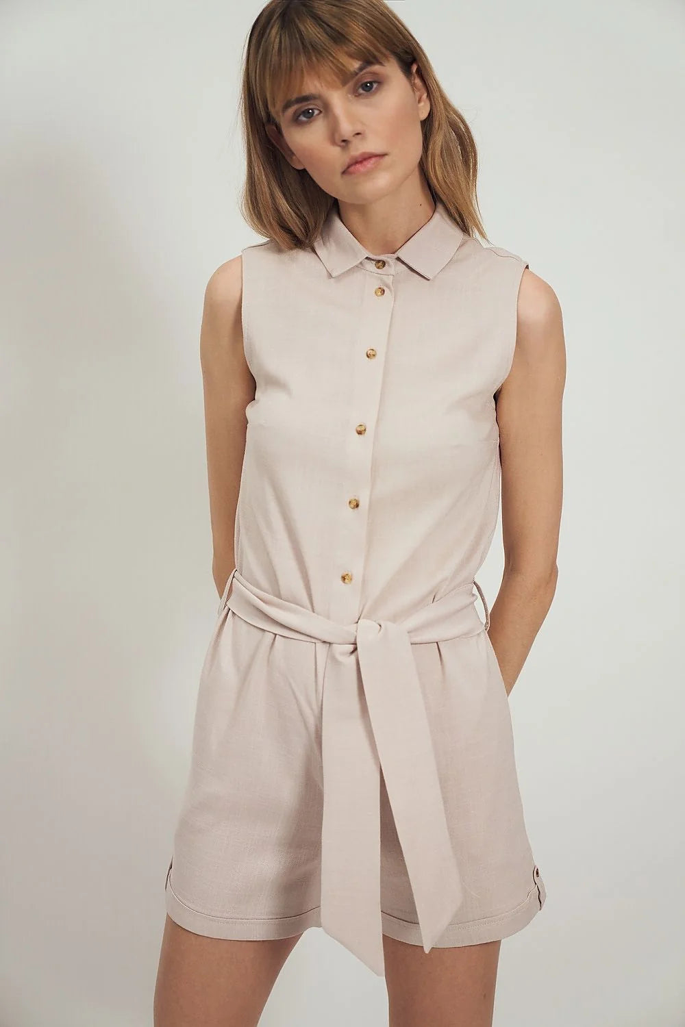 Combinaison sans manches moderne pour femme, style épuré, coupe droite, col chemise, fermeture à boutons dorés, tissu léger respirant, couleur neutre, waist cintré, shorts au-dessus du genou, occasion estivale, look chic décontracté