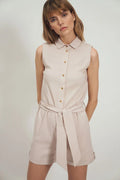 Combinaison sans manches moderne pour femme, style épuré, coupe droite, col chemise, fermeture à boutons dorés, tissu léger respirant, couleur neutre, waist cintré, shorts au-dessus du genou, occasion estivale, look chic décontracté