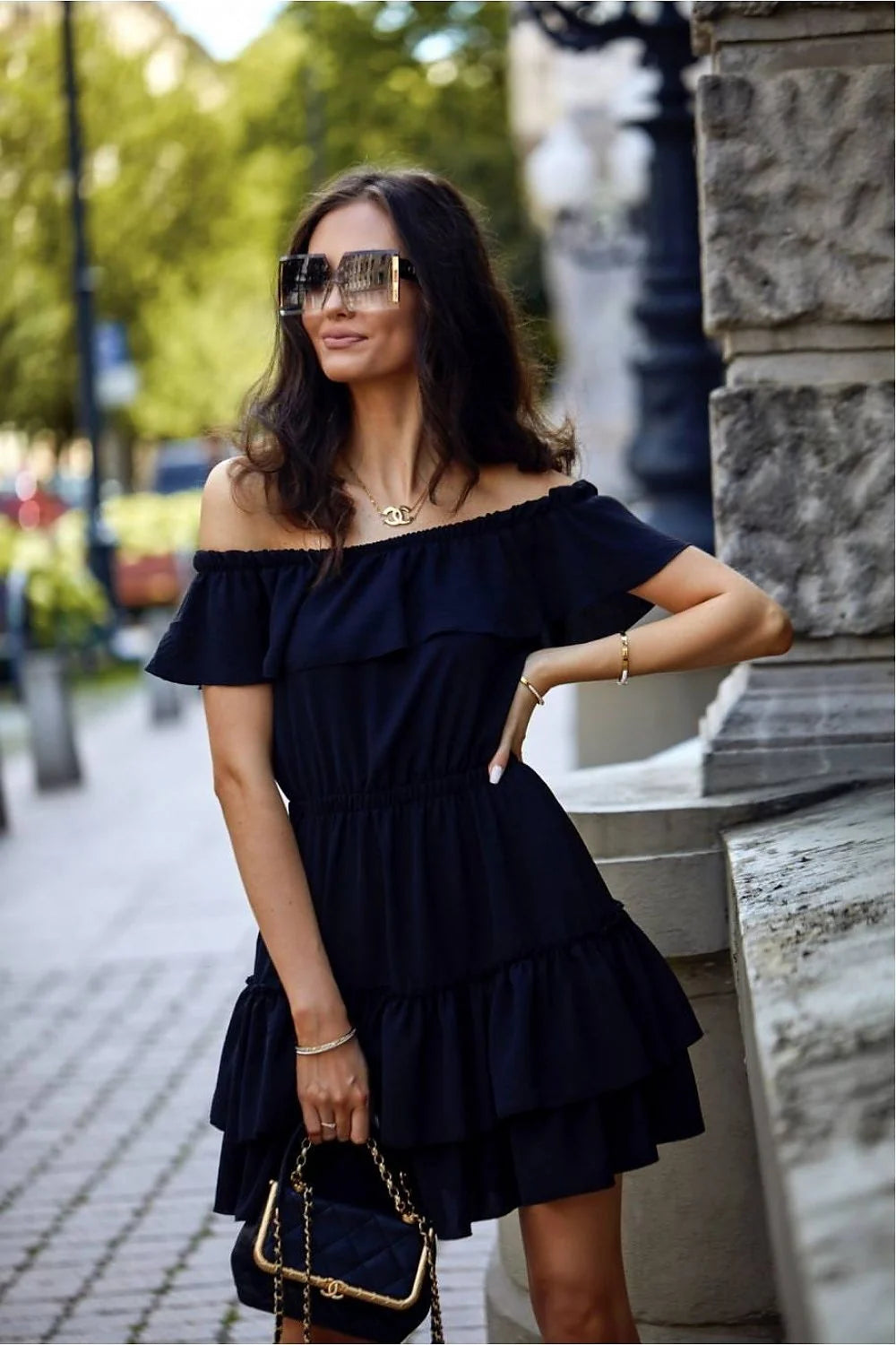 Robe de jour Roco Fashion épaules dénudées volants tissu lisse taille ajustable couleur noire porté avec sac à bandoulière sandales femmes occasion estivale